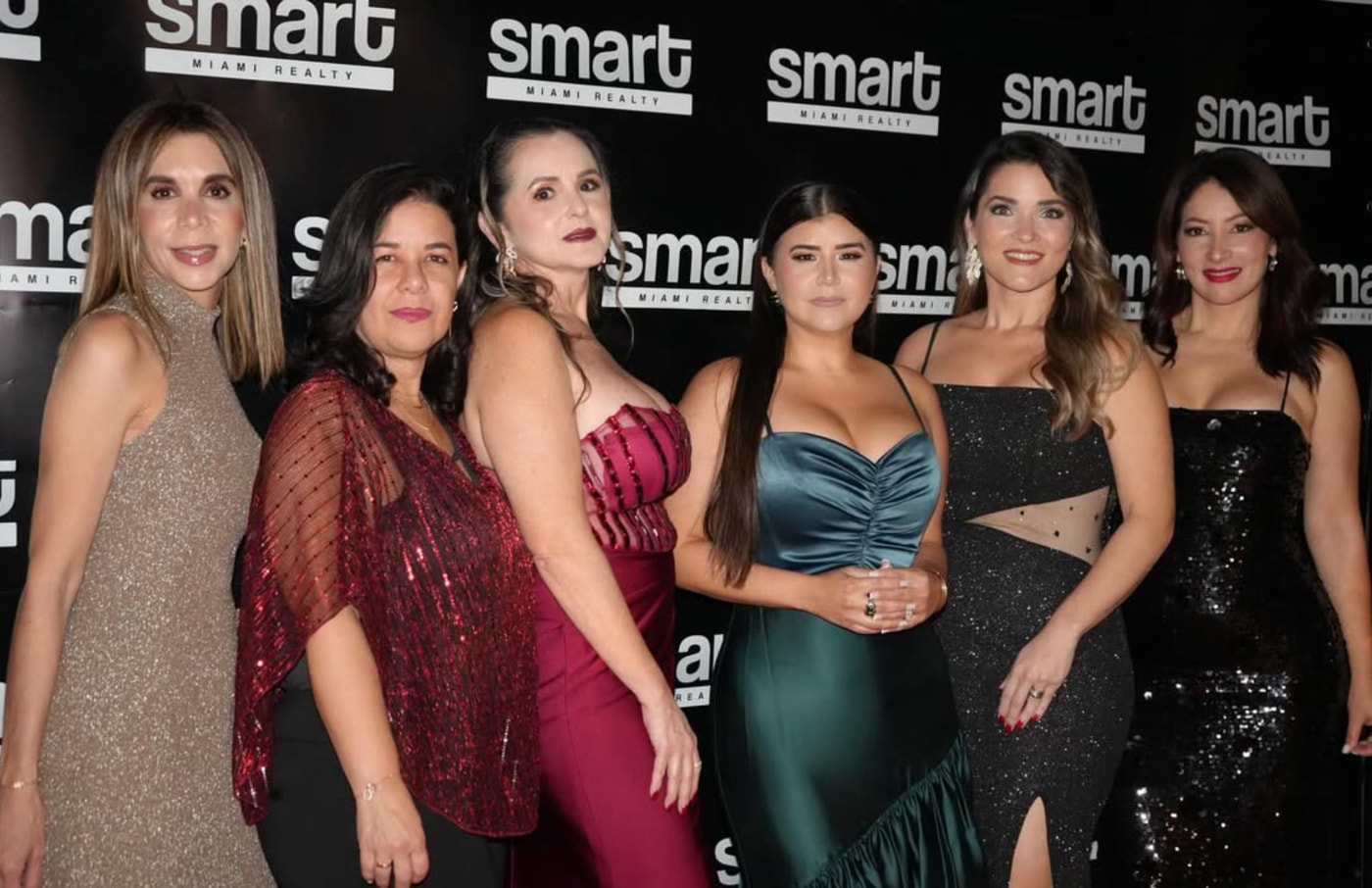 Six people celebrating together at a Smart Miami Realty event in front of a branded backdrop.